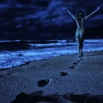 Person walking on a beach at night with arms raised, leaving footprints in the sand.