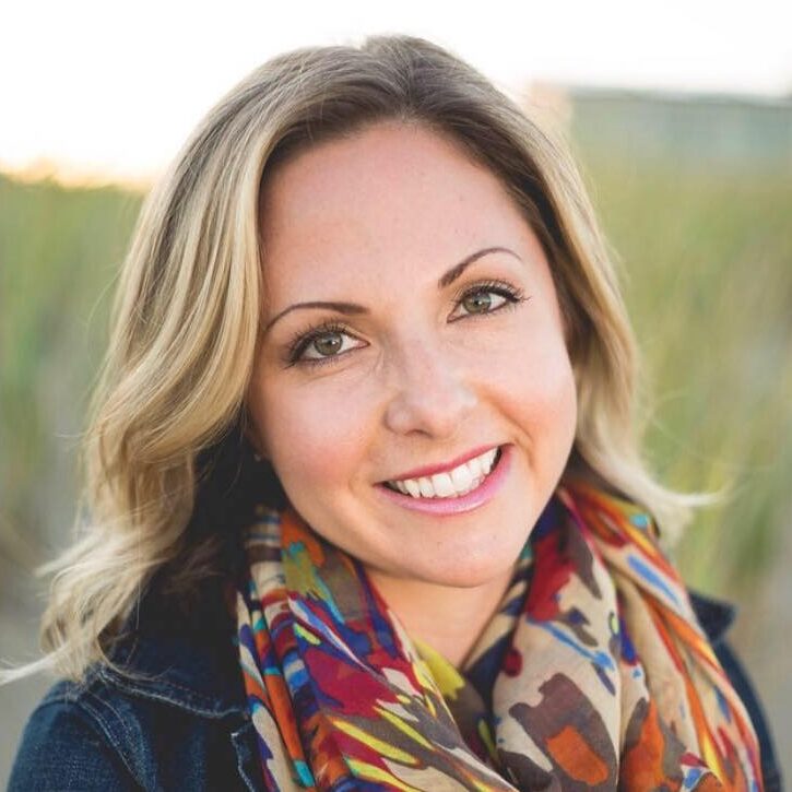 Emily-Aarons-1 Client testimonial image featuring Emily Aarons with wavy blonde hair, wearing a denim jacket and colorful scarf, smiling in the outdoors.