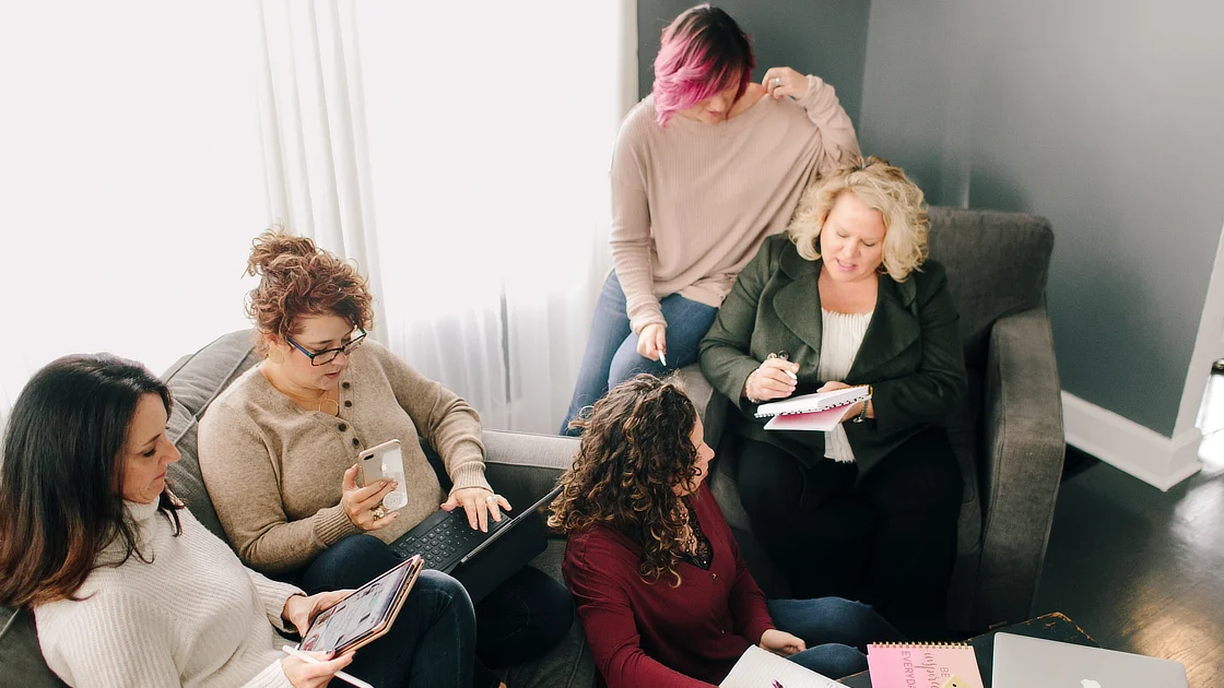 Kim Woods Business Strategist with Group of Clients Kim Woods and a group of clients gathered in a cozy setting during an in-person retreat. They are engaged in discussion, taking notes, and using laptops and tablets.