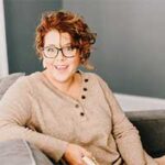 start here Stacy Ziegler sitting comfortably on a couch, featured in a client testimonial for Kim Woods’ intuitive leadership guidance.