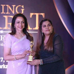 Testimonials Vandana Tolani receives an award on stage, standing with another woman, both holding a trophy and smiling at the camera.