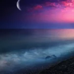 A peaceful seaside at dusk, with gentle waves lapping against the shore, a crescent moon high in the sky, and shades of pink and purple blending in the horizon.