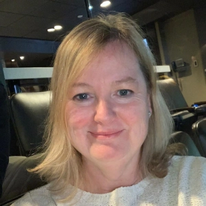 Sue Ewer in a light sweater, seated in a cozy, softly lit indoor space.