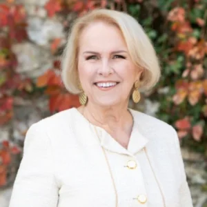 Kim Woods Master Astrologer Client testimonial Dr Dorothy Martin-Neville Dr. Dorothy Martin-Neville smiling outdoors in a cream-colored jacket with gold earrings, standing in front of a stone wall with autumn leaves.