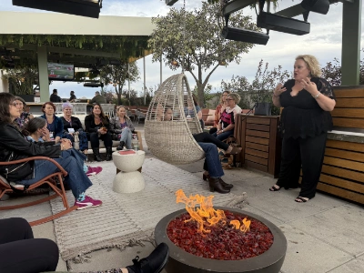 Kim Woods speaking to a circle gathered around a fire pit during a full moon ritual, inviting transformation and release.