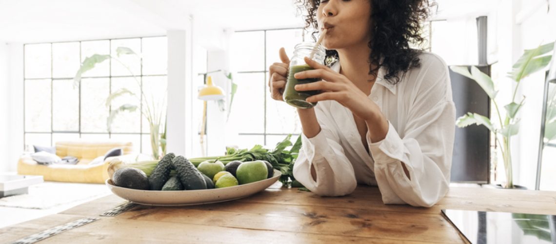 Young african american woman drinking green juice with reusable bamboo straw in loft apartment. Copy space