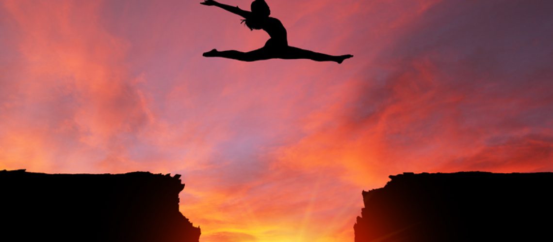 Silhouette of girl dancer in a split leap over dangerous cliffs with dramatic sunset or sunrise background and copy space. Concept of faith, conquering adversity, taking risk; challenge, courage, determination or achievement.  Please note the sunset background was shot in Calgary on 10-24-2017 (reference image attached).  The dancer model was shot in studio on 04-07-2016 (Reference image attached and Model Release also attached). The dance model was isolated in Photoshop and then composited onto the sunset background as a silhouette.